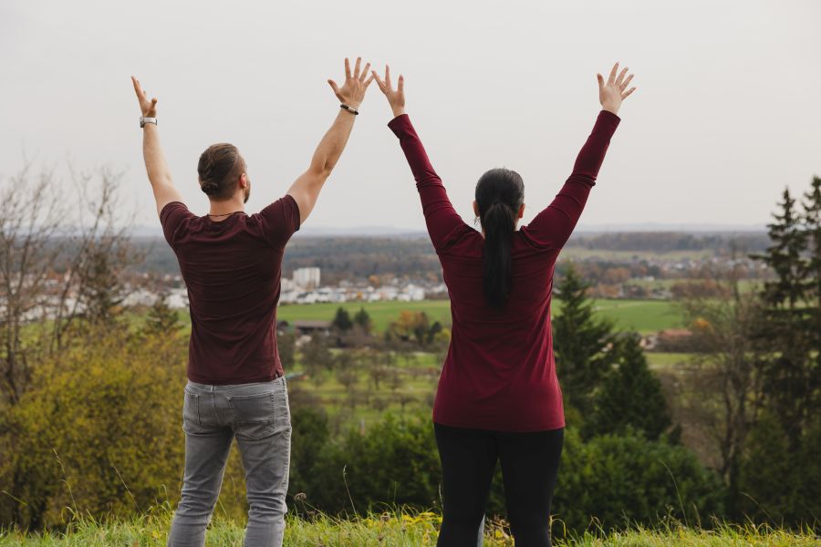 Mann und Frau stehen nebeneinander, sie sind von hinten sichtbar, die Arme sind nach oben au ausgestreckt