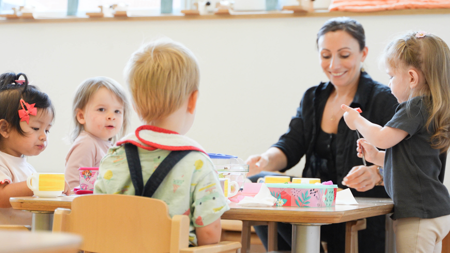 Kita-Mitarbeiterin mit Kindern am Tisch Kita-Mitarbeiterin mit Kindern am Tisch